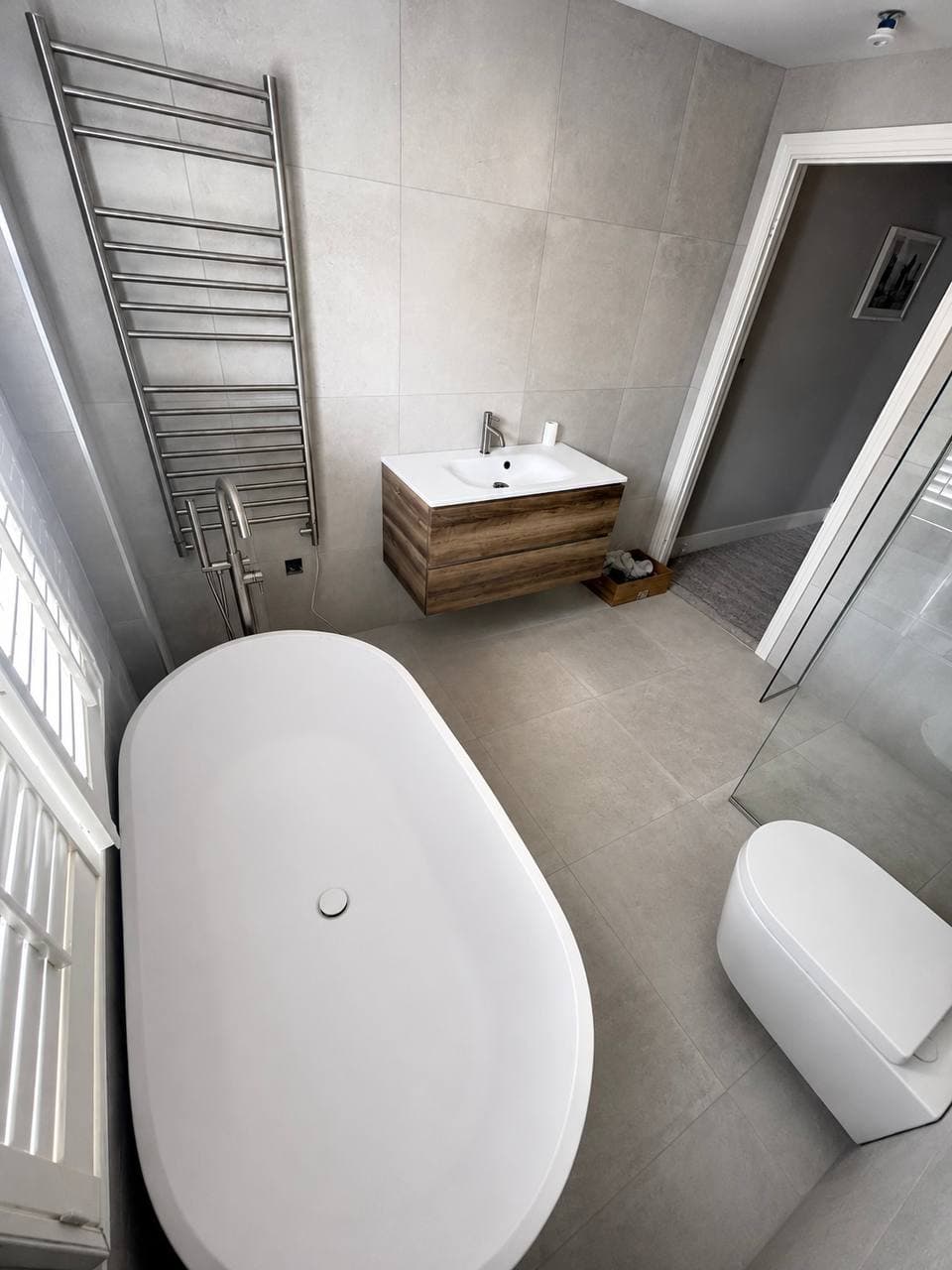 Freestanding bath with wall-mounted wooden vanity and brushed metal fittings