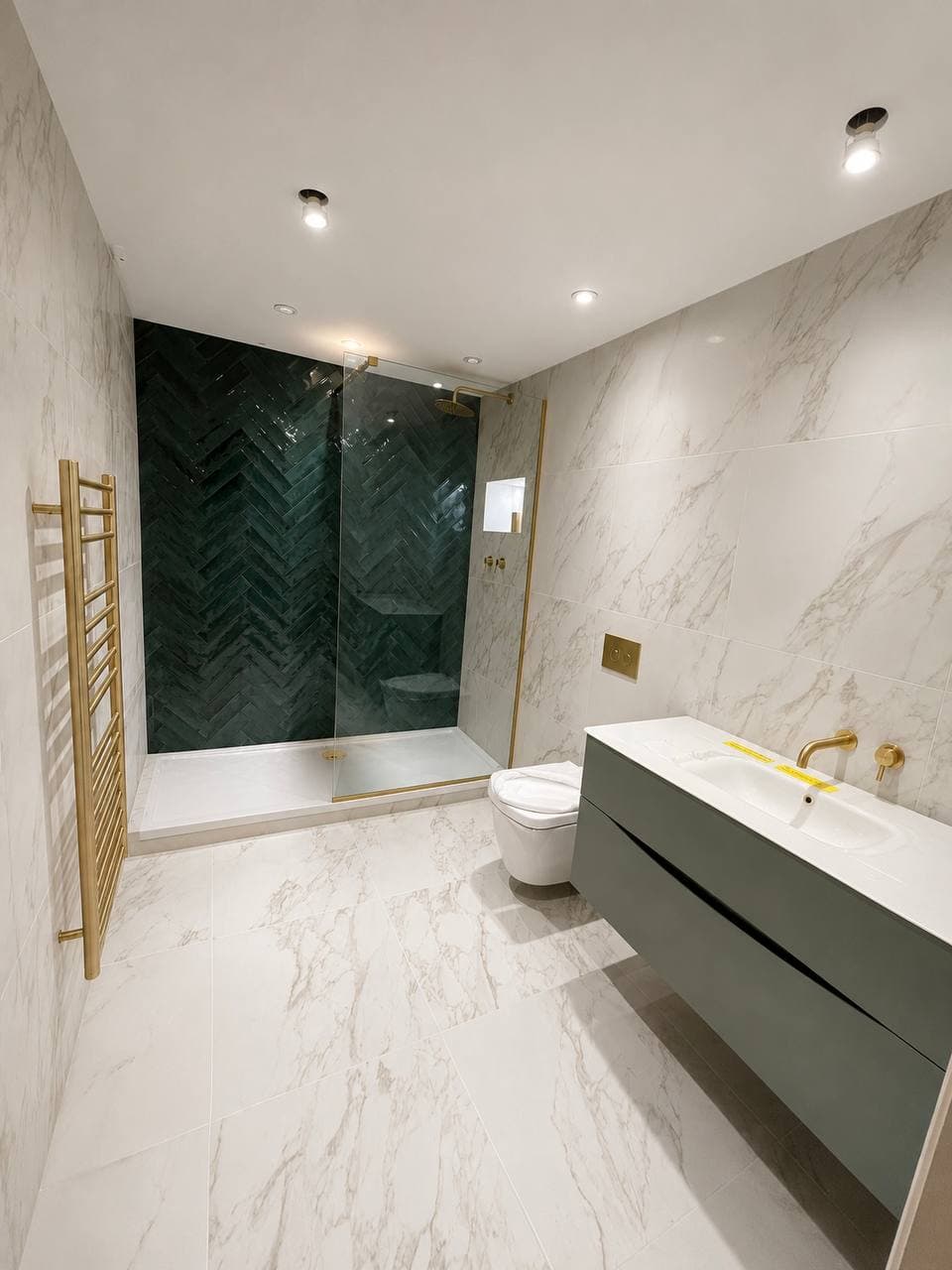 Bathroom with marble-effect tiling, green herringbone shower wall, wall-mounted vanity and brushed brass fittings