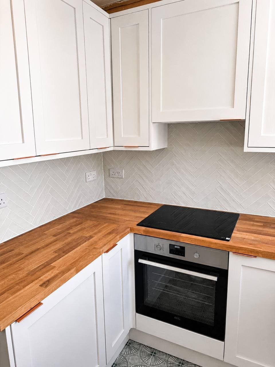 Finished kitchen with neutral cabinetry, timber worktop, black hob and herringbone tiled splashback