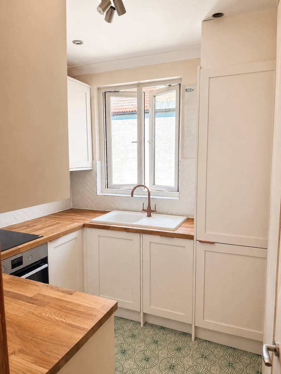 Finished compact kitchen with warm neutral cabinetry, timber worktops and patterned flooring